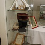 Dans cette vitrine, du haut vers le bas. - Photographie de Clémence Brunet, infirmière major - Maquette : infirmière dans son poste de secours - Le képi du médecin Félix Michaud - Un certificat d'origine fourni par la famille Michaud - Broc de métal émaillé, utilisé pour les soins aux blessés .